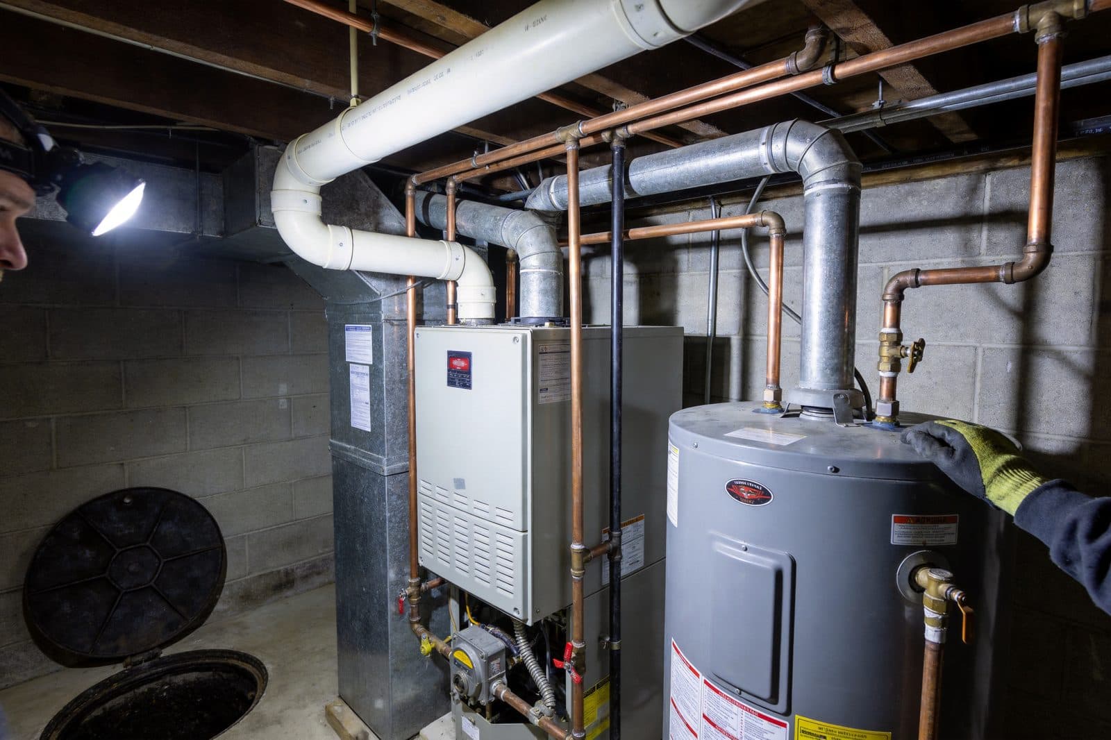 A furnace and hot water tank in a basement lit by a headlamp